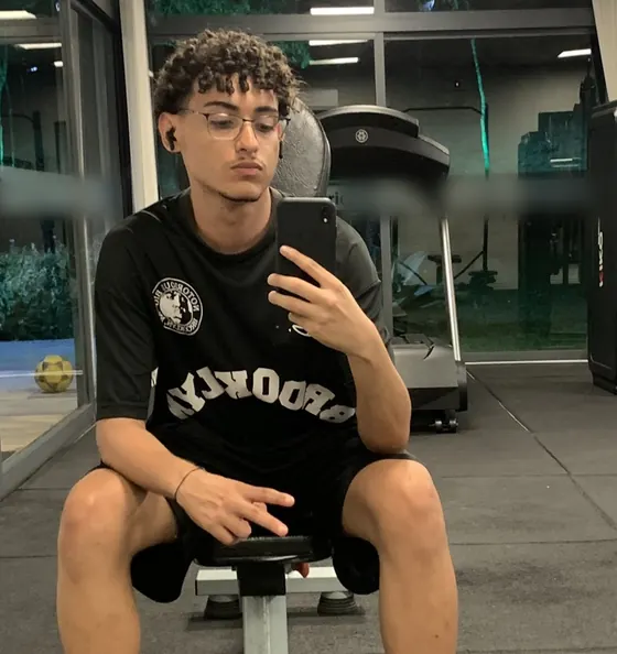 Gustavo sentado num banco da academia, tirando foto no espelho